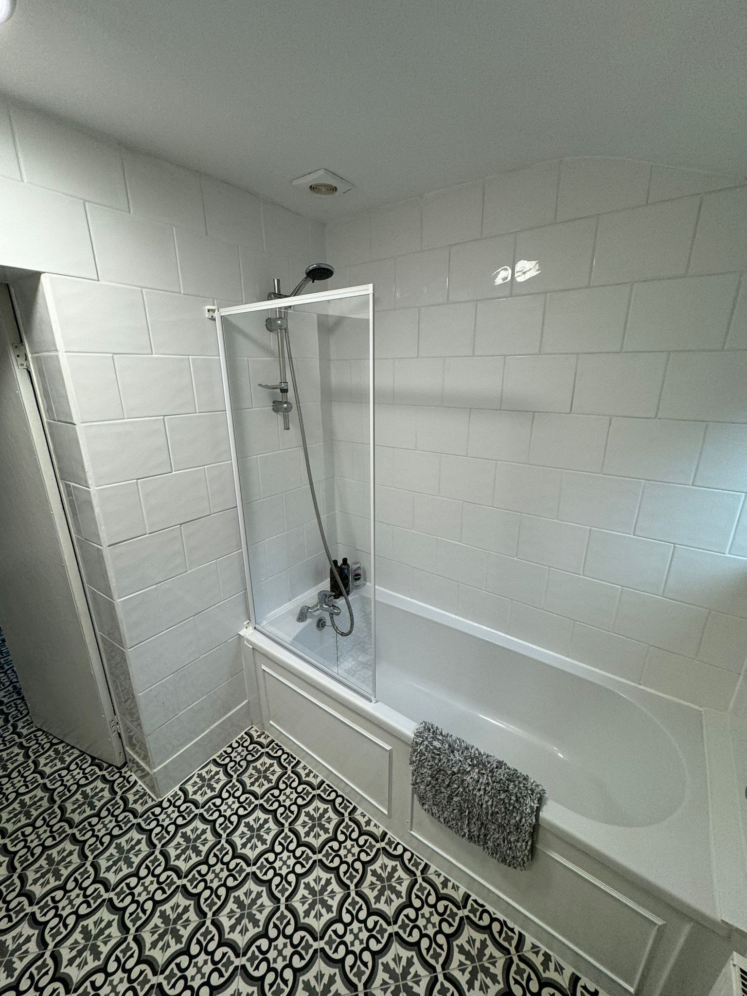 A bathroom with a shower enclosure, a bathtub, and patterned floor tiles.