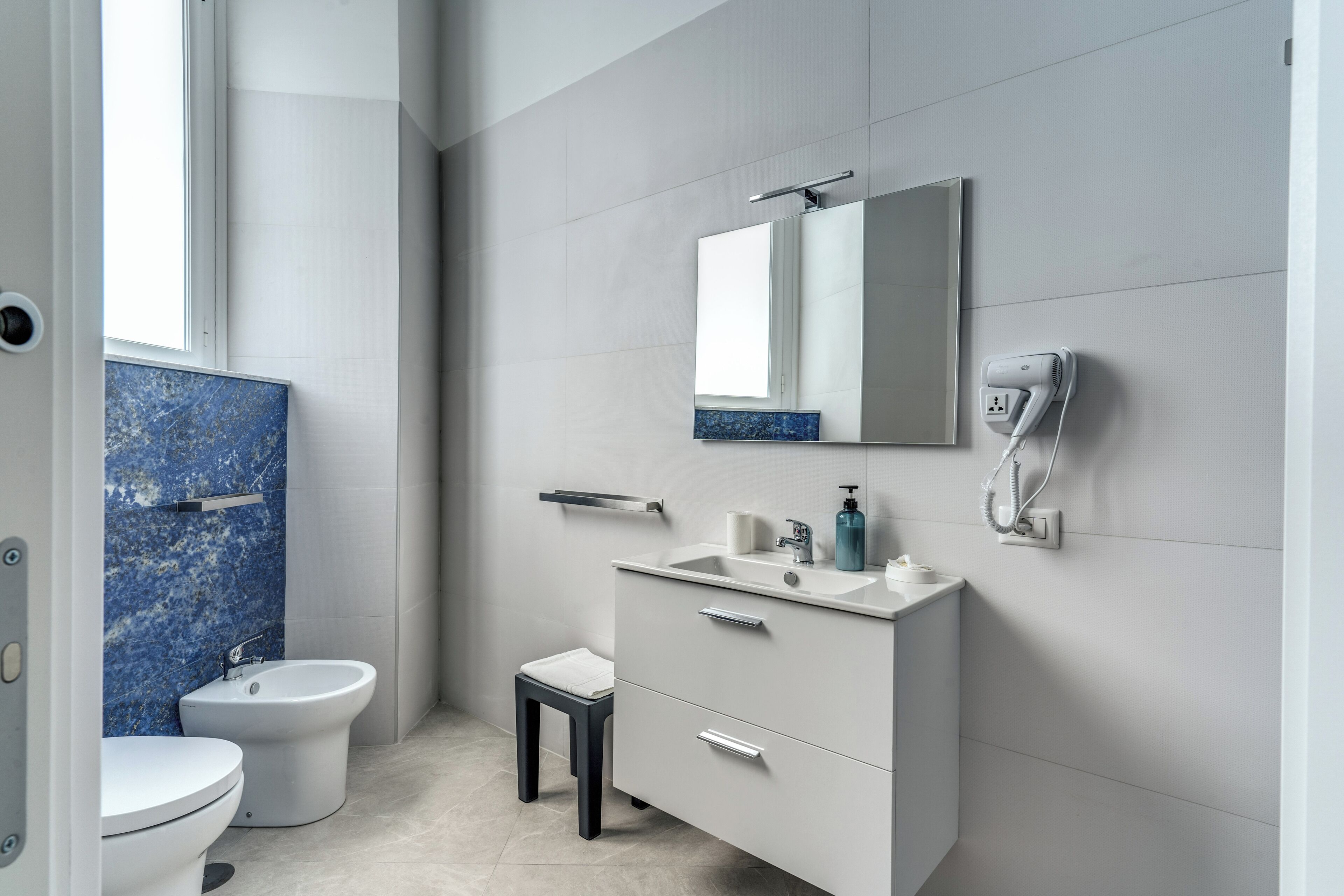 A modern bathroom with a toilet, bidet, vanity with a mirror, and a hairdryer on the wall.