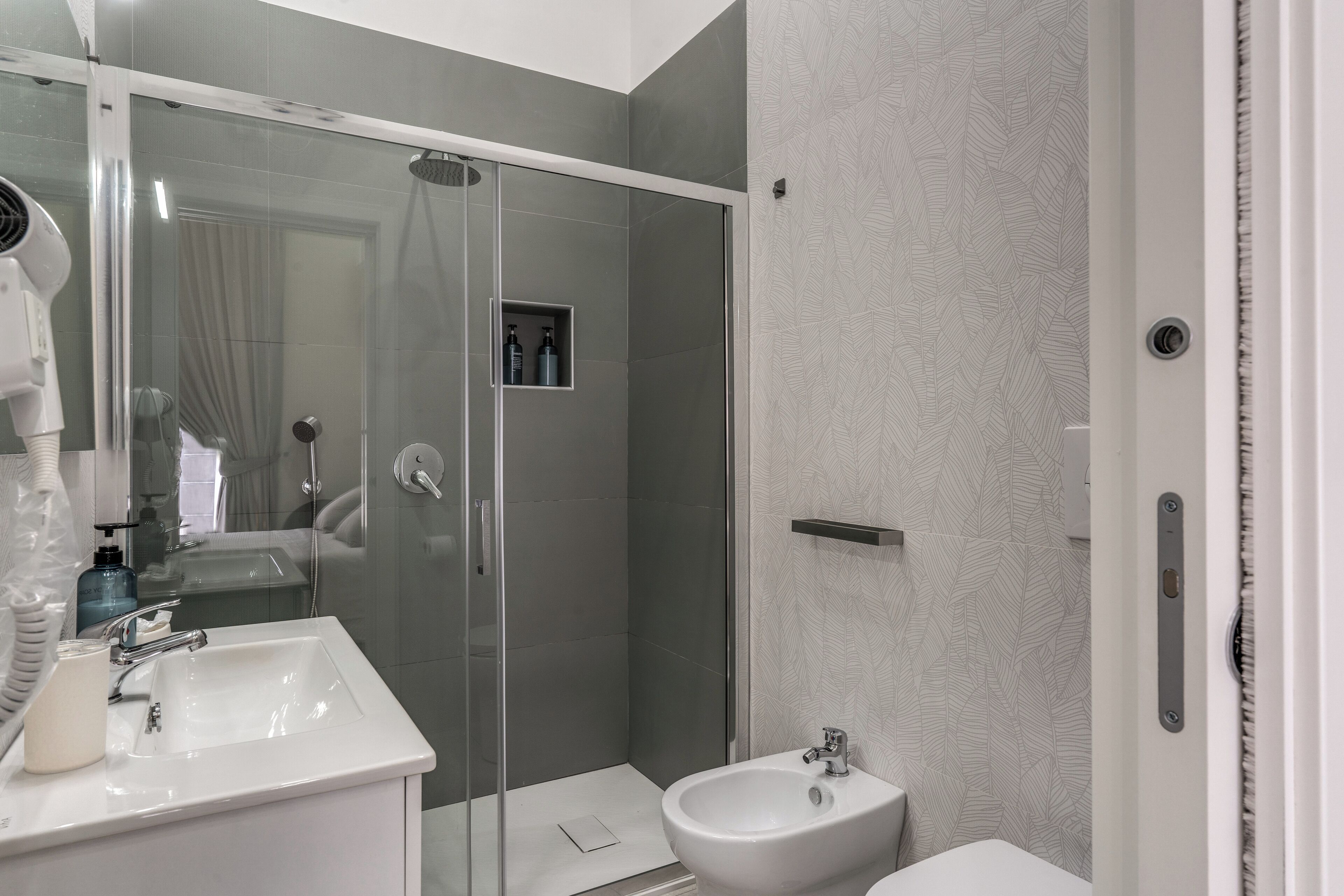 Un baño moderno con ducha de vidrio, un lavamanos blanco y un bidé.