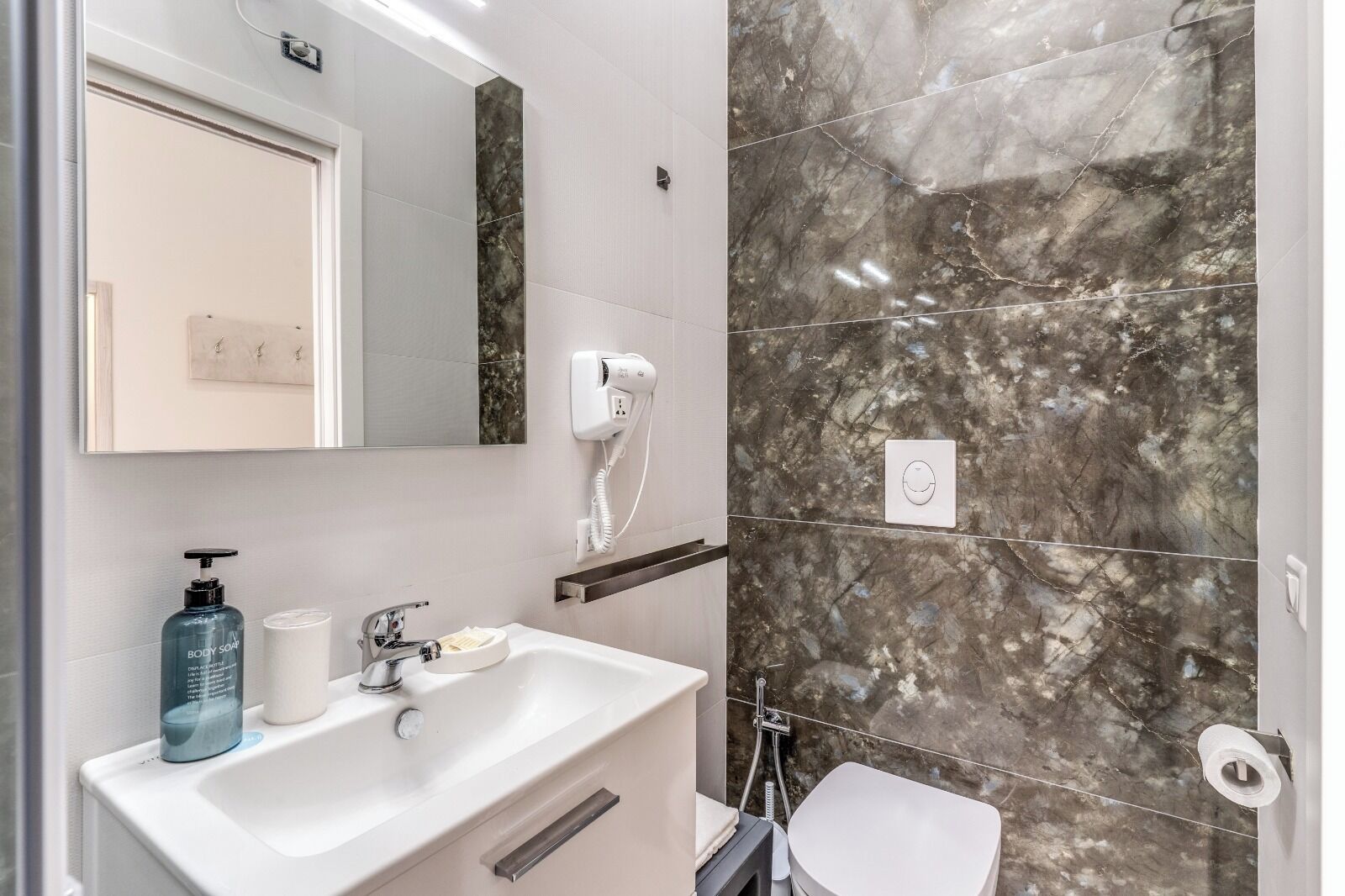 A modern bathroom with a white sink, a hairdryer, and a marble wall.