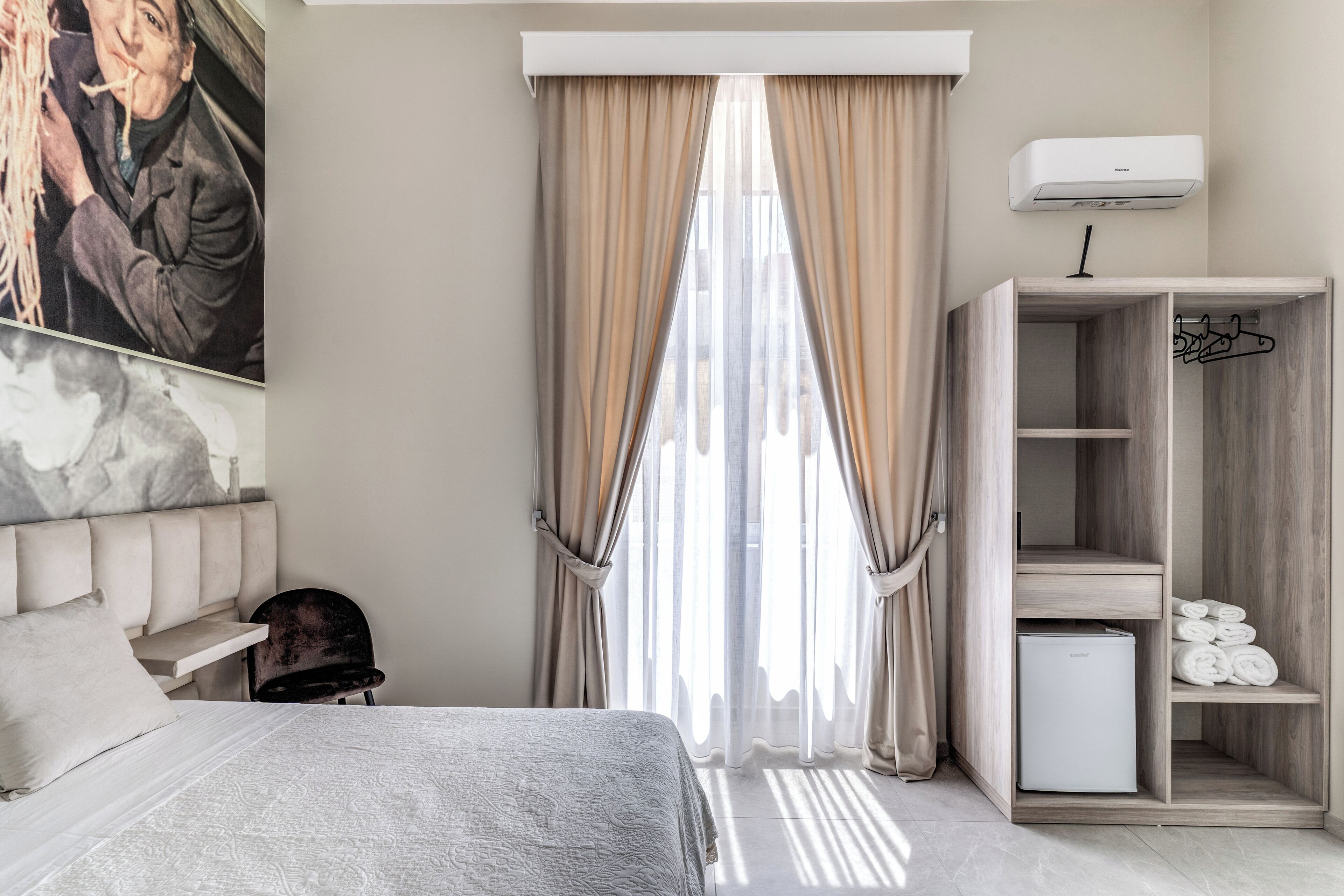 A hotel room with a bed, a desk, a chair, a wardrobe, and a window with curtains.