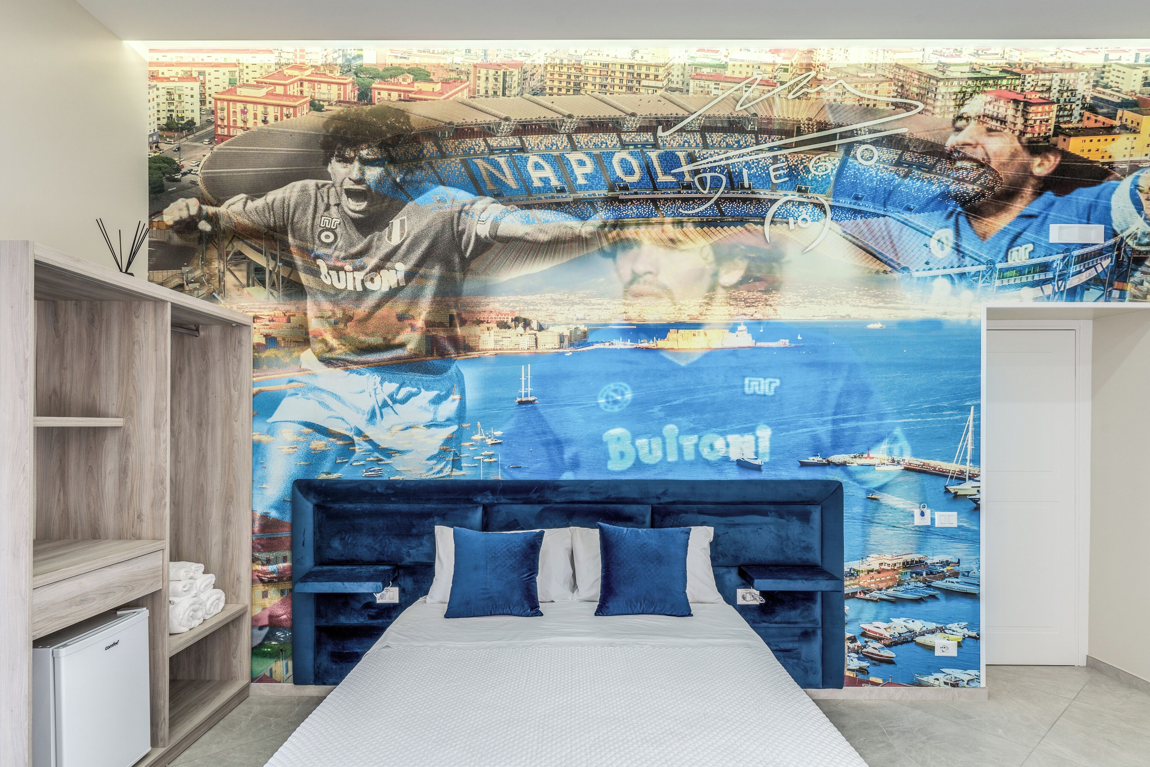 Un dormitori amb un mural d'un paisatge urbà i un llit amb roba de llit blava.