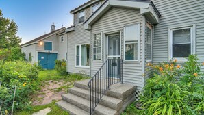 A two-story house with a front porch, a blue garage door, and a small garden with flowers and plants. - Lakefront Maine House ~ 4 Mi to Colby College (Oakland)