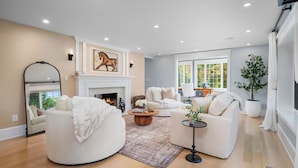 A spacious living room with a fireplace, two white sofas, a round coffee table, and a large mirror. - Family getaway.Commuter's Dream.Weddings&Events.Content House.Luxury Smart Home (Larchmont)