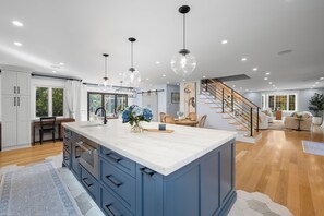 A modern kitchen with a large island, wooden flooring, and pendant lighting.
