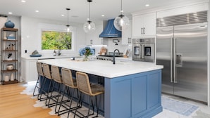 A modern kitchen with a large island, stainless steel appliances, and a blue accent wall. - Family getaway.Commuter's Dream.Weddings&Events.Content House.Luxury Smart Home (Larchmont)