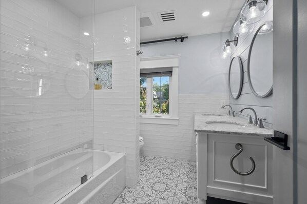 A modern bathroom with a glass-enclosed shower, a freestanding bathtub, a vanity with a sink, and a window providing a view of the outdoors.