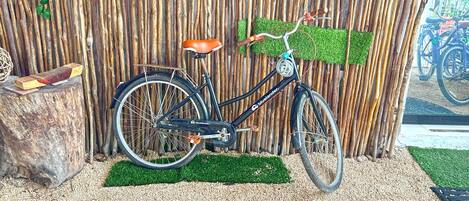 Uma bicicleta encostada em uma cerca de bambu, com um tapete de grama sintética verde à frente.