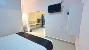 A bedroom with a bed, a TV mounted on the wall, and a view into the kitchen area. - Soi Bacalar (Bacalar)