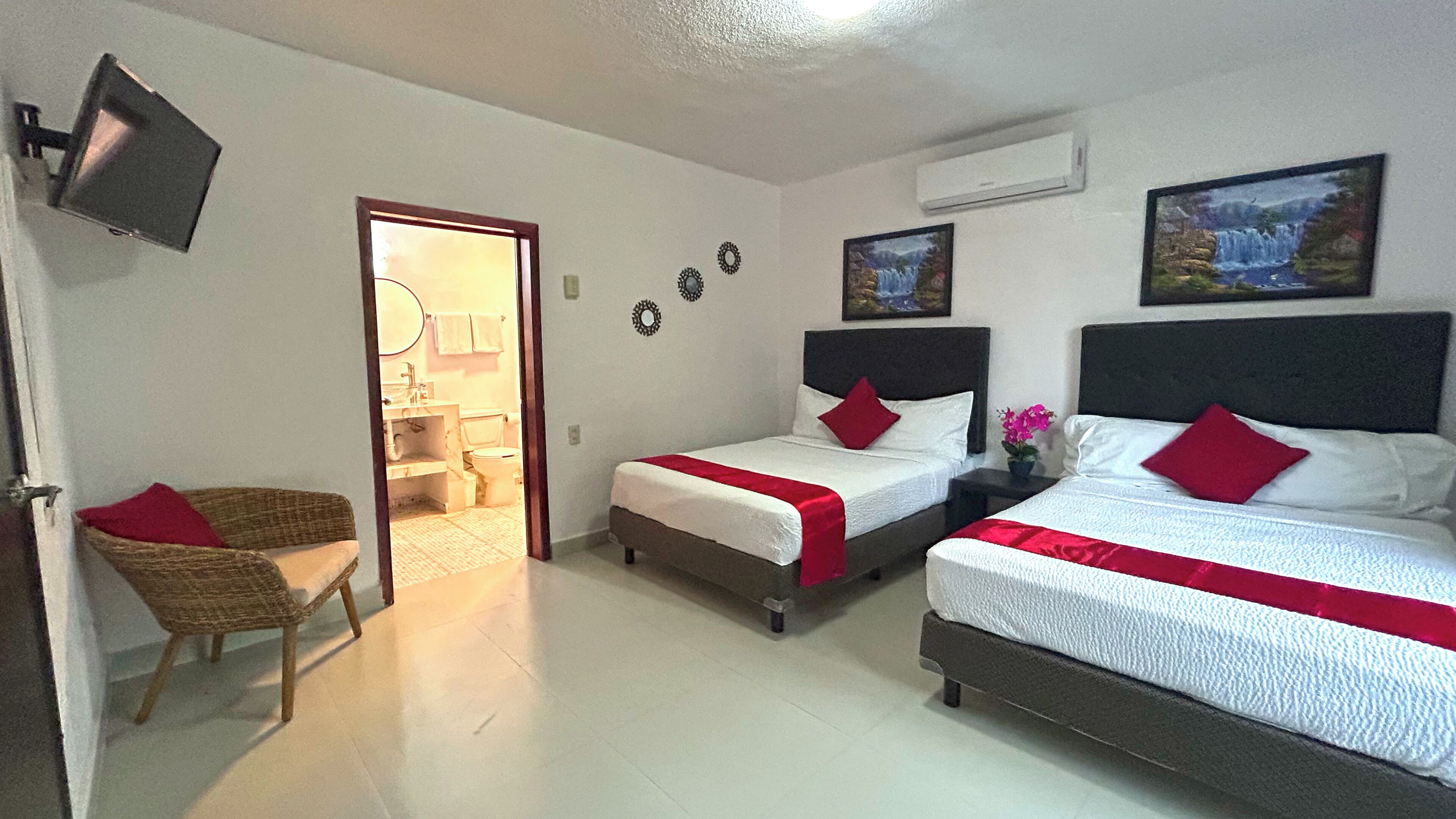 A hotel room with two beds, a television, a chair, and a bathroom visible through an open door.