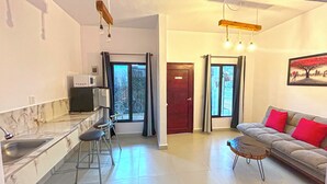 A modern kitchen with a built-in microwave, a dining area with a bar stool, a sofa with red cushions, and a painting on the wall. - Soi Bacalar (Bacalar)