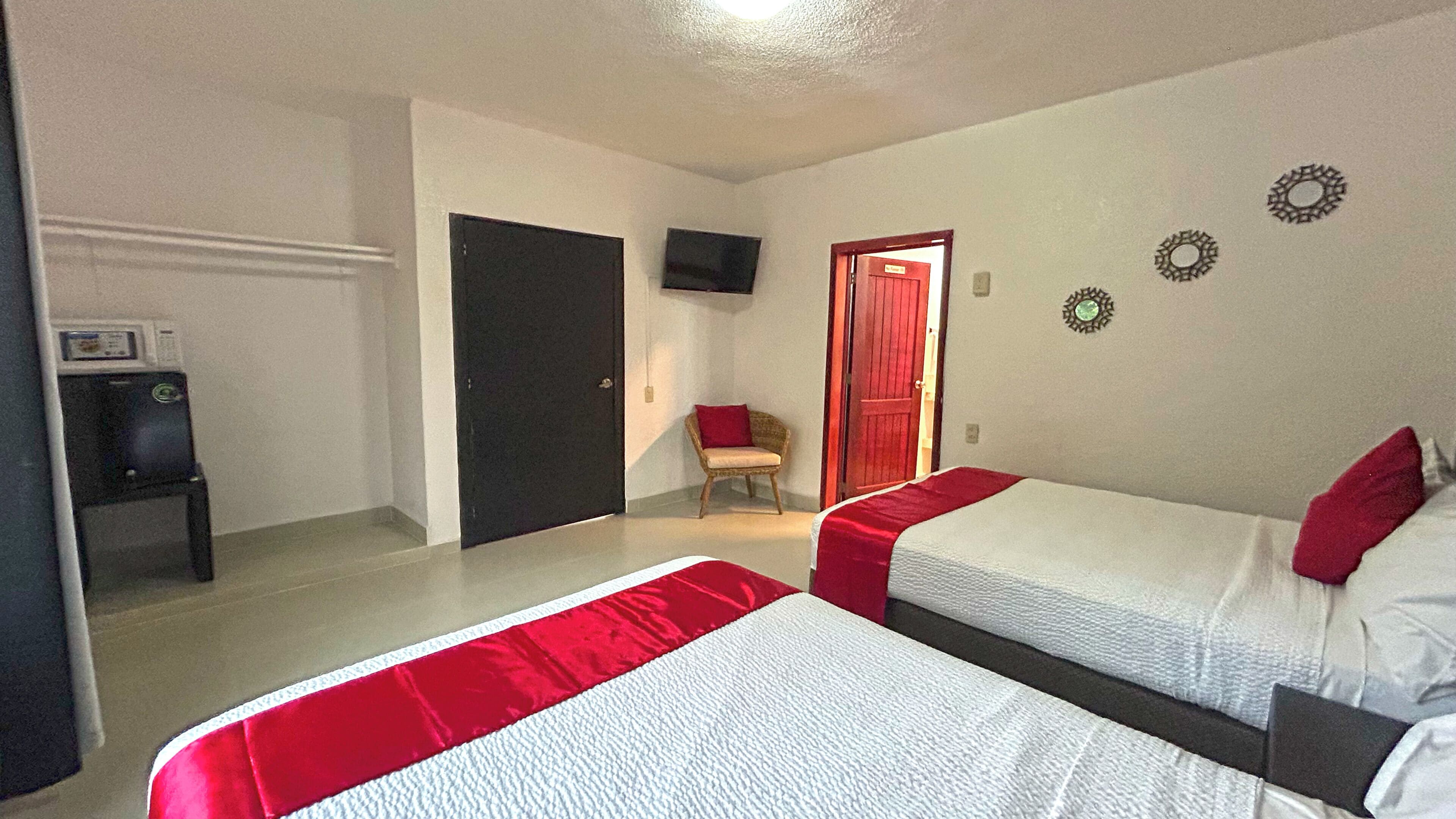 Quarto de hotel com duas camas, televisão, uma cadeira e uma porta.