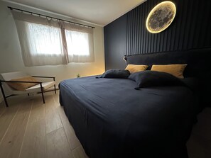 Un dormitorio moderno con una cama, una silla, un ventanal con cortinas y una lámpara de pared.
