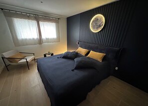 Et moderne soveværelse med en seng, en stol, et sengebord og en vægmonteret lampe.