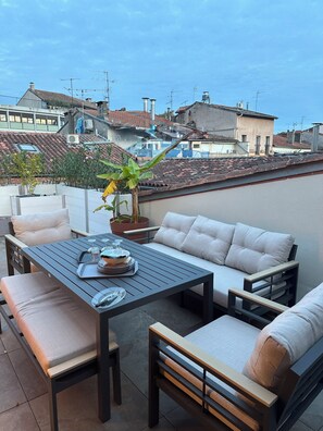 Una terrazza esterna con tavolo da pranzo, sedute imbottite e piante in vaso.