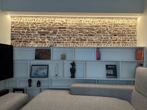 Una sala de estar con pared de ladrillo, estanterías blancas y un televisor.