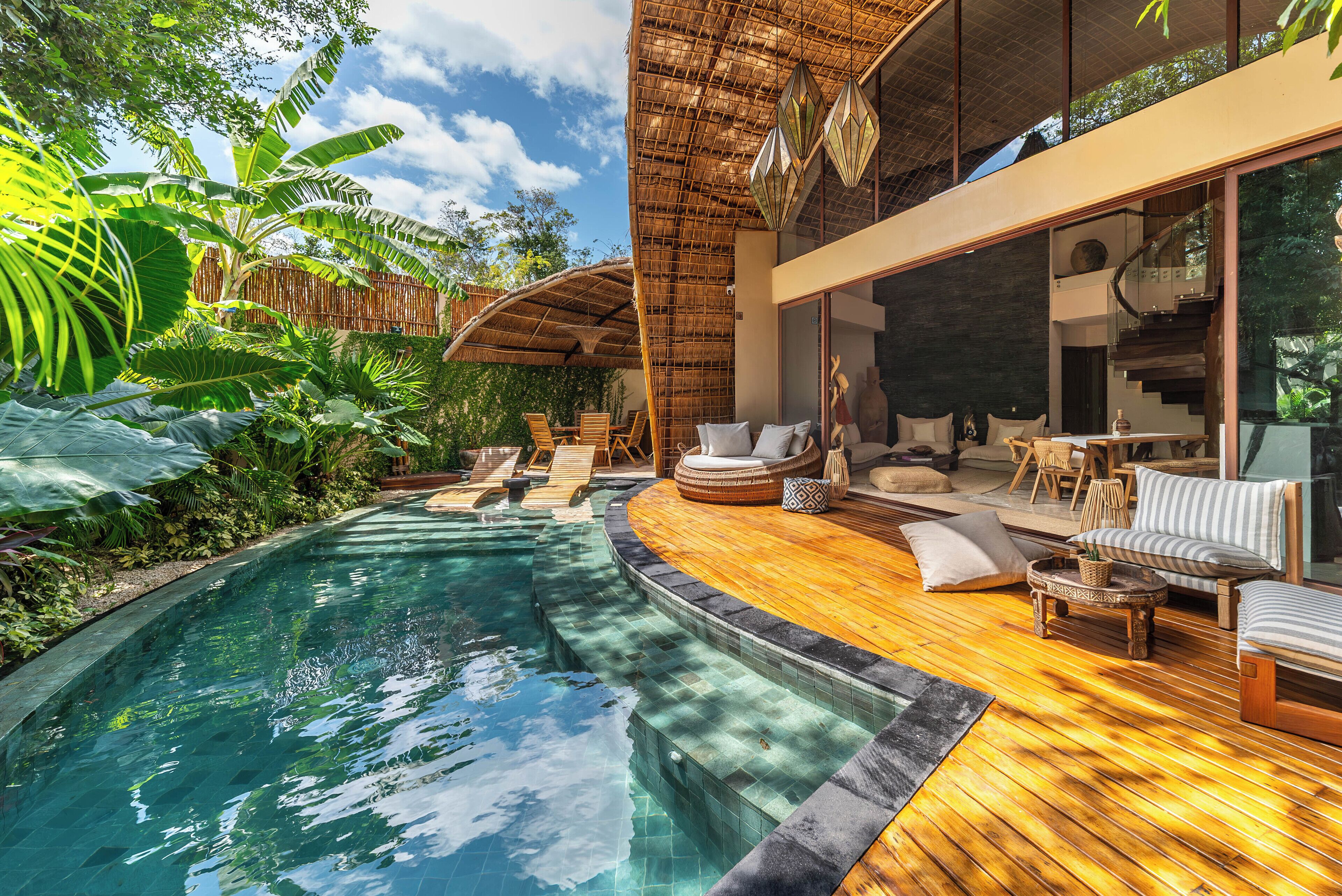 Ein moderner Poolbereich im Freien mit einer Holzterrasse, Liegestühlen und einer großen Glasdoor, die zu einem Wohnbereich führt.