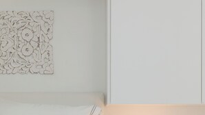 Une chambre à coucher au style minimaliste, avec un lit, une table de chevet dotée d’une lampe et un élément décoratif mural.
