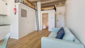 Un appartement moderne avec une chambre en mezzanine, une cuisine et un espace de vie doté d’un canapé bleu clair.