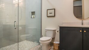 A bathroom with a glass shower enclosure, a toilet, a sink with a dark cabinet, and a framed picture on the wall.