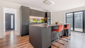 A modern kitchen with a central island, two bar stools, and a large sliding glass door to the outdoors.