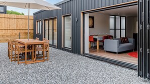 A modern house with a patio area featuring a wooden table and chairs, a large umbrella, and a gravel floor.