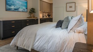 A bedroom with a bed, a nightstand, a dresser, a painting, a plant, and a kitchen area. - Luxury Downtown Loft (Athens)