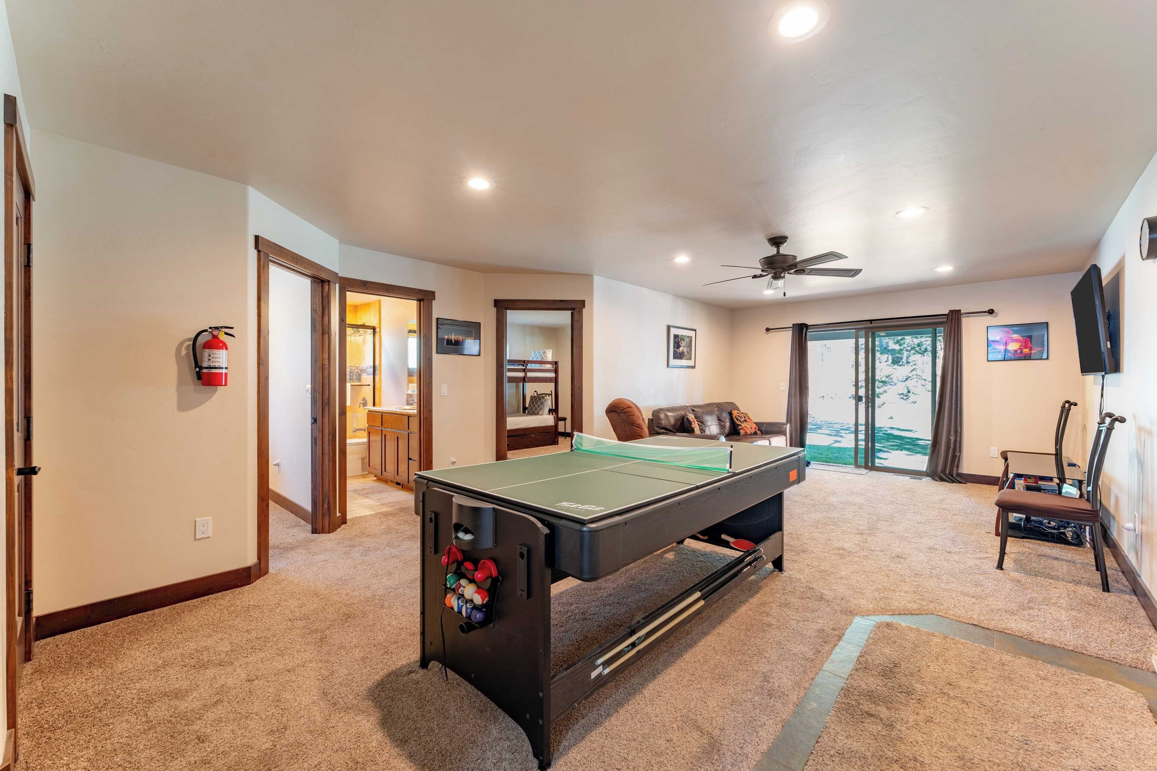 A room with a pool table, a ceiling fan, a fire extinguisher, and a door leading to another room.