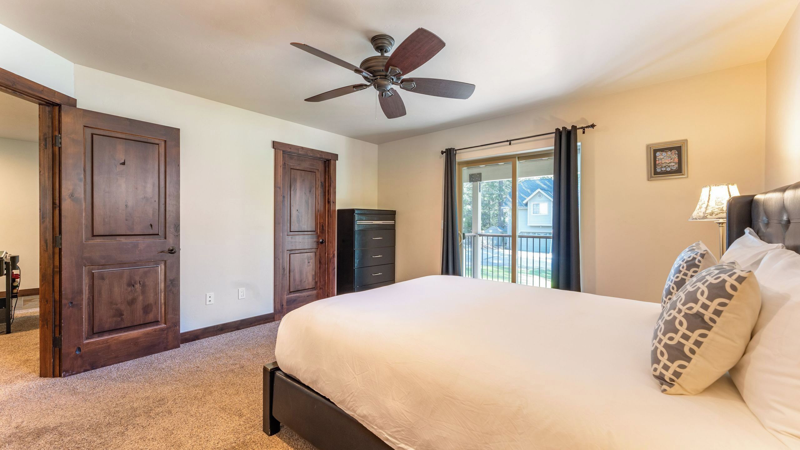 A bedroom with a bed, a ceiling fan, a dresser, and a window with curtains.