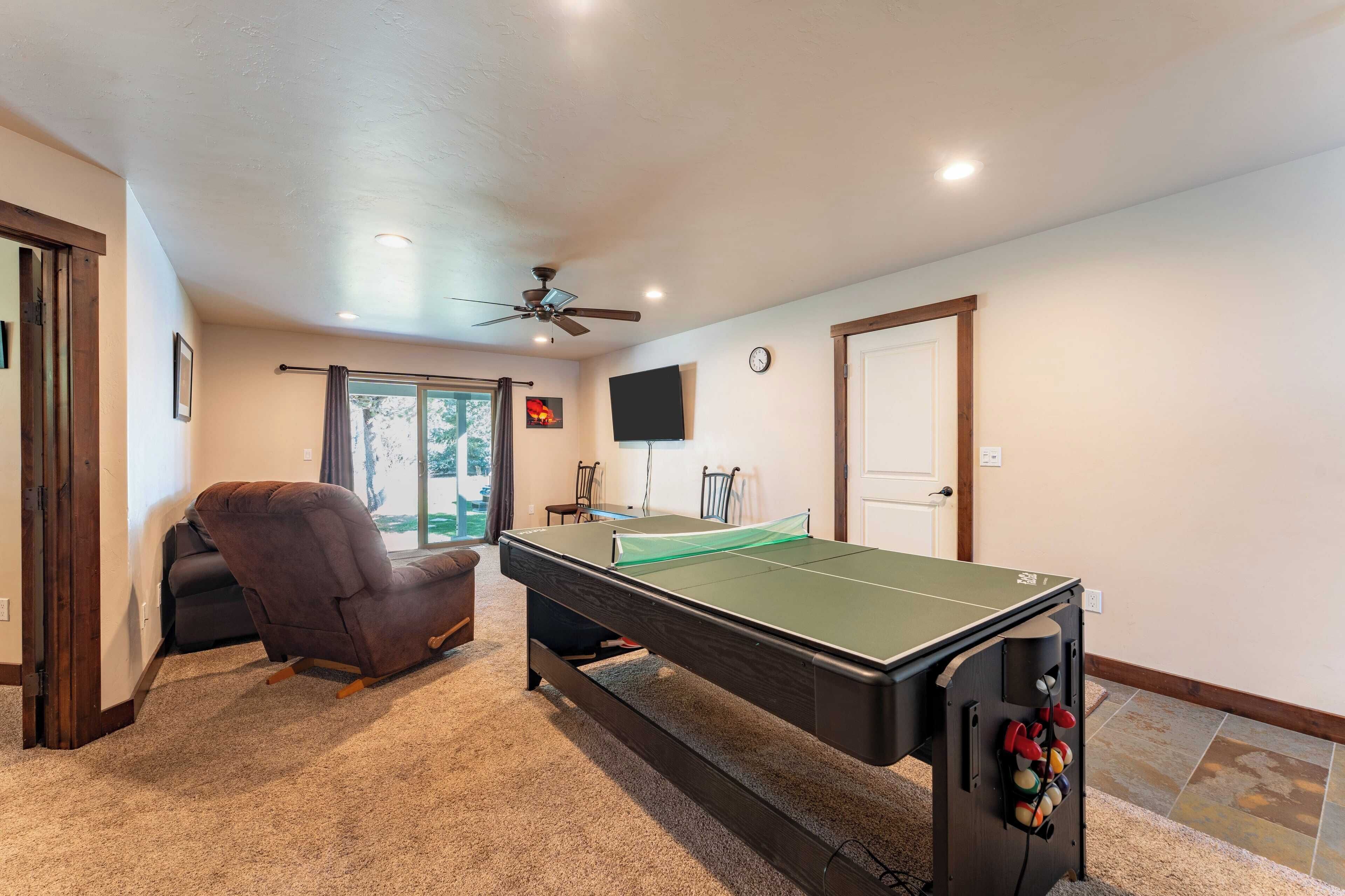 A room with a pool table, a ceiling fan, a TV, and a door.