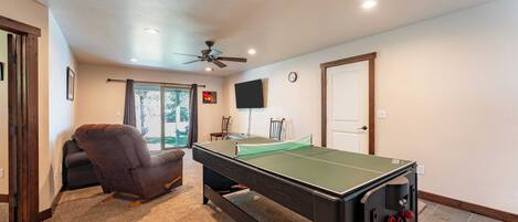 A room with a pool table, a ceiling fan, a TV, and a door.