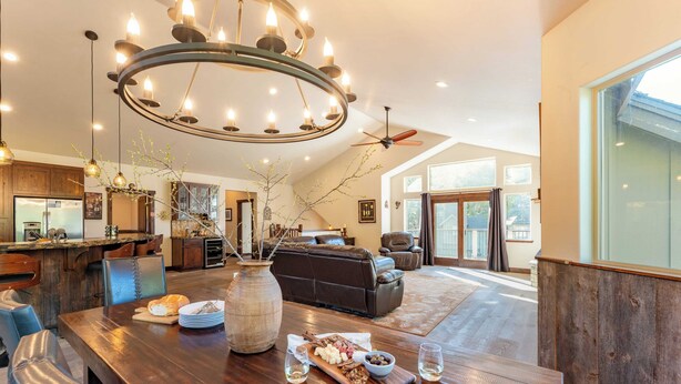 A spacious living area with a large wooden dining table, a chandelier, and a modern kitchen in the background. - 10mins to Lake Hot Tub, Game Room, Forest Views Meyers Meadow by Avantstay (South Lake Tahoe)