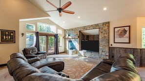 A spacious living room with a stone fireplace, leather sofas, a flat-screen TV, and a ceiling fan. - 10mins to Lake Hot Tub, Game Room, Forest Views Meyers Meadow by Avantstay (South Lake Tahoe)