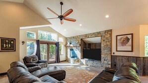 A spacious living room with a stone fireplace, leather sofas, a ceiling fan, and a large flat-screen TV. - 10mins to Lake Hot Tub, Game Room, Forest Views Meyers Meadow by Avantstay (South Lake Tahoe)