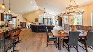 A modern kitchen with a bar area, a dining table with chairs, and a large window providing natural light. - 10mins to Lake Hot Tub, Game Room, Forest Views Meyers Meadow by Avantstay (South Lake Tahoe)
