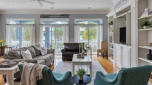A spacious living room with a grey sofa, teal armchairs, a coffee table, and a TV on a white cabinet. - Crabline Getaway by Avantstay Private Pool + Hot Tub Easy Beach Access (Hilton Head Island)