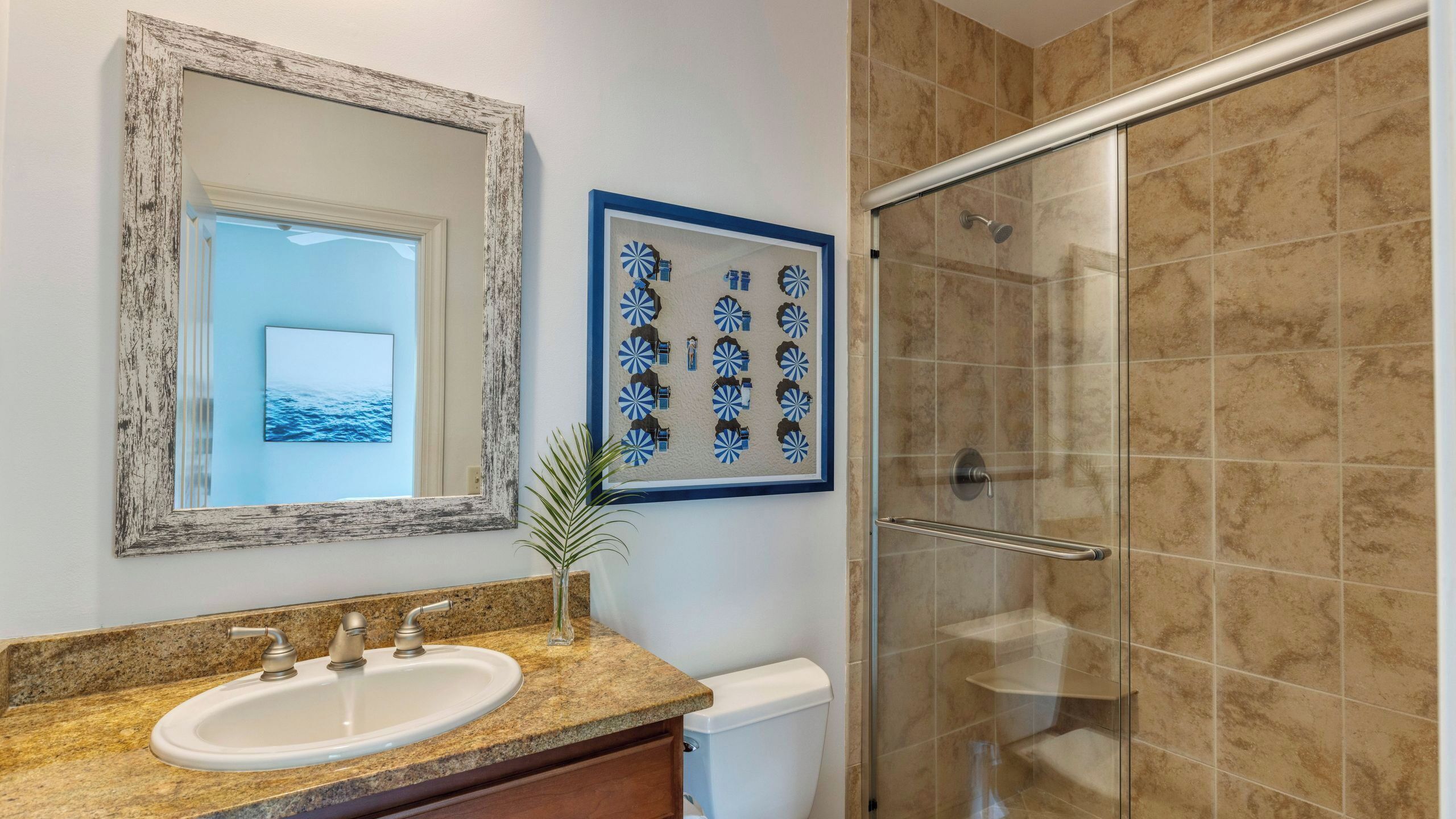 Une salle de bain équipée d’un lavabo, d’un miroir, d’une œuvre d’art encadrée et d’une douche.