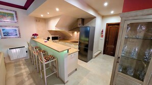 Une cuisine compacte équipée d’un réfrigérateur encastré, d’un four à micro-ondes et d’une cuisinière. On y trouve également des tabourets de bar et un petit évier.
