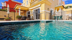 Une piscine à l’eau claire, entourée de mobilier d’extérieur et d’un bâtiment doté de balcons.