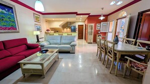 Un salon avec un canapé rouge, une table basse en verre et un coin repas comprenant des chaises et une table en bois.