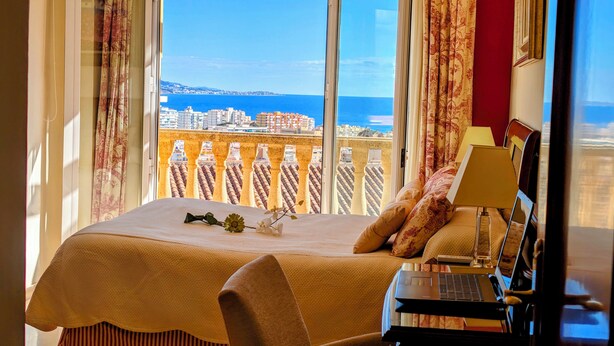 Une chambre d’hôtel avec un lit, un ordinateur portable et une vue sur la mer et le paysage urbain.