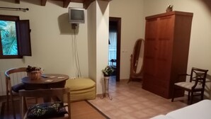 A room with a bed, a wooden wardrobe, a small table with a basket, a chair, and a television mounted on the wall. - La Canal (Santillana del Mar)