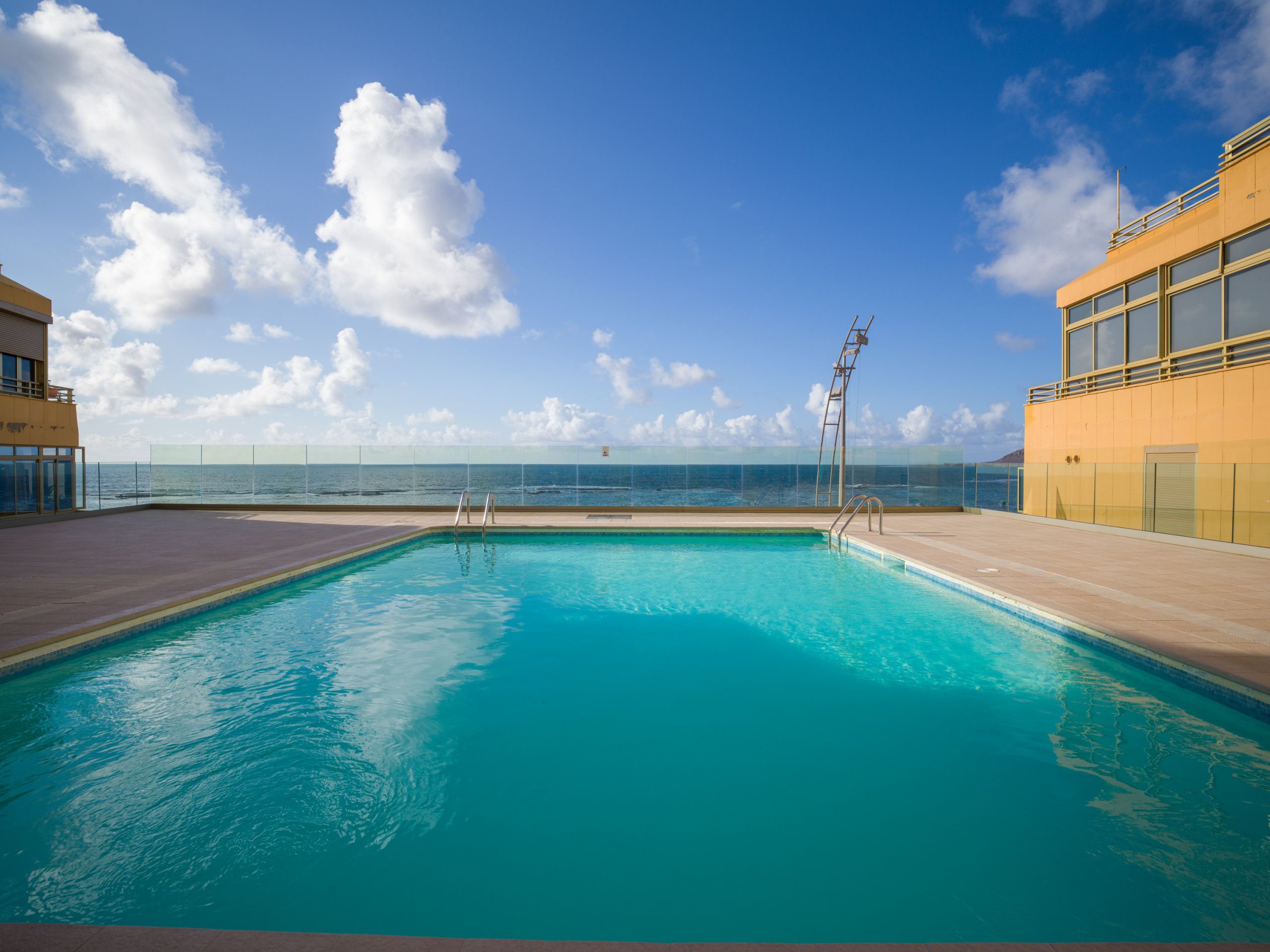 Ein klares, blaues Schwimmbecken mit Blick auf den Ozean und einen wolkenlosen Himmel.