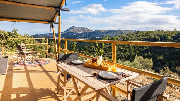 A wooden deck with a table set for breakfast, overlooking a mountainous landscape. - Glamping Chania - Secluded Oasis Among the Trees (Tsivaras)