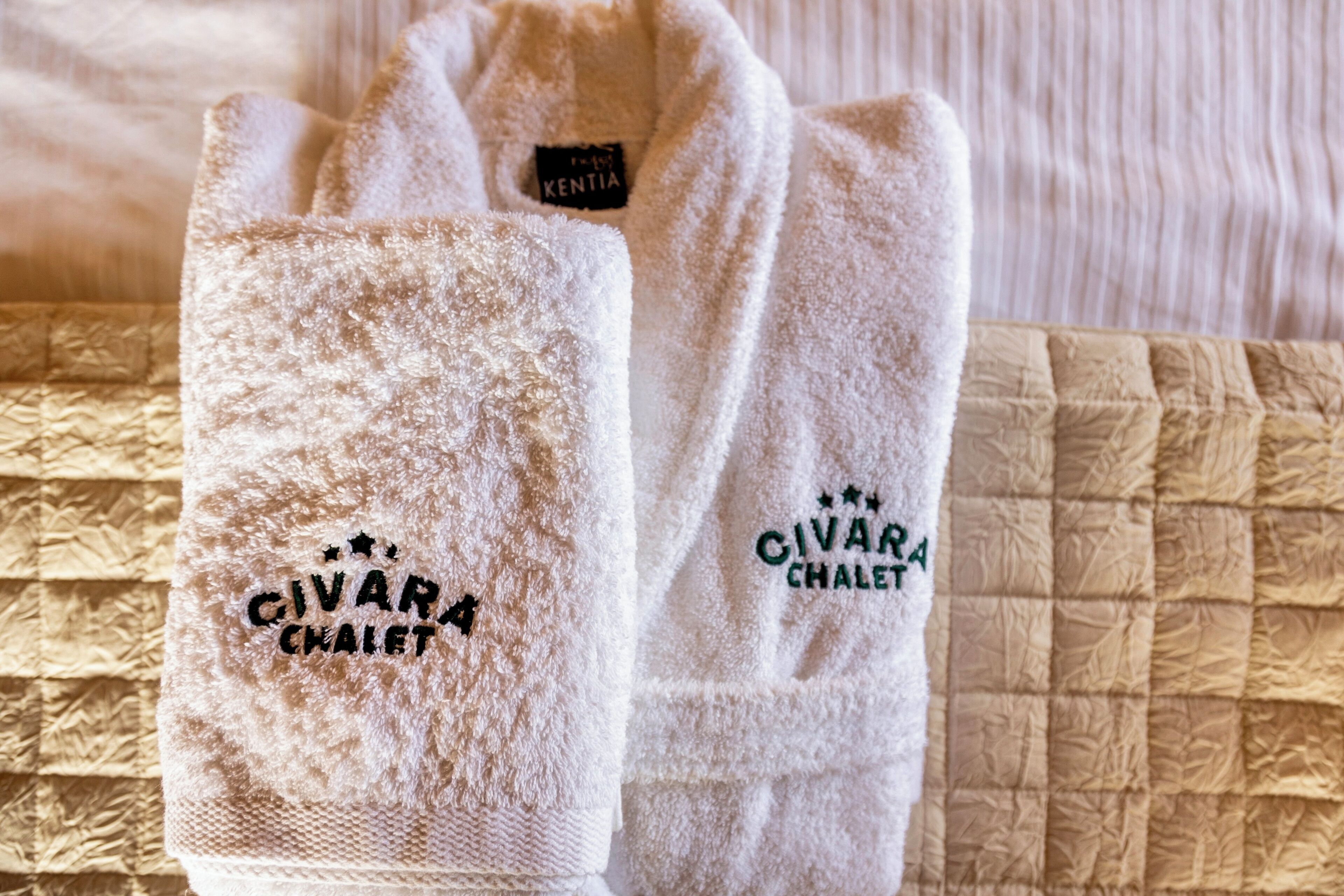 A pair of white towels with embroidered text "CIVARA CHALET" on a textured surface.