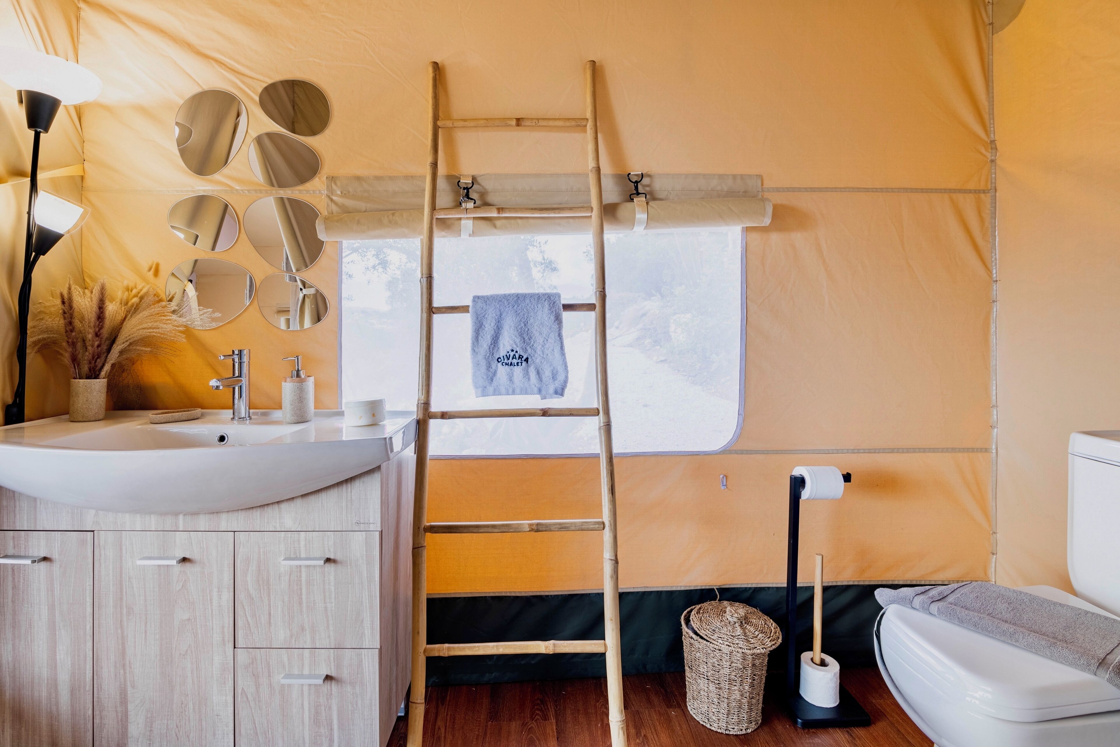 A compact, well-organized tent bathroom with a sink, mirror, ladder, and toilet.