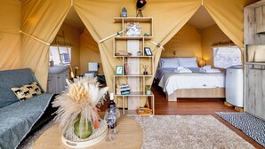 A cozy tented accommodation with a central shelving unit, a bed, a sofa, and a dining area. - Glamping Chania - Secluded Oasis Among the Trees (Tsivaras)