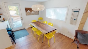 A dining area with a wooden table and yellow chairs, a hanging light fixture, and a window with a view. - ASPEN GROVE / Fernie / Hot Tub/ Walk Downtown (Fernie)