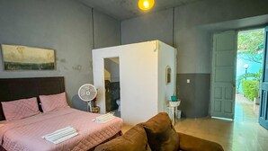 Ein Schlafzimmer mit einem Bett, einem braunen Ledersessel, einem Standventilator und einer Deckenleuchte.