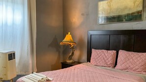 Ein Hotelzimmer mit einem Bett, einem Nachttisch, einer Lampe, einem Gemälde und einem Fenster mit Vorhängen.